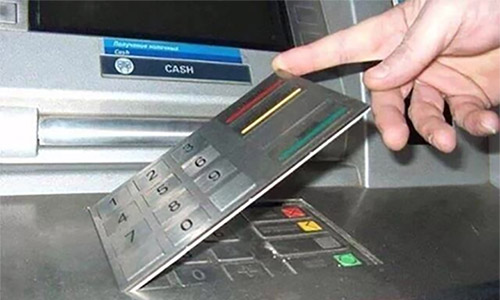 person lifting a skimmer keypad that was placed on top of an ATM keypad